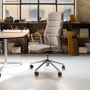Sillón That’s it Executive de Quinti con brazos fijos de aluminio junto a una mesa de despacho