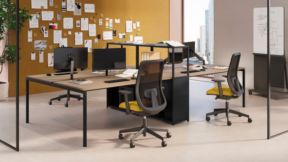 Puestos Sigma de Las Mobili enfrentados, sillas de malla con asiento amarillo y pared de corcho